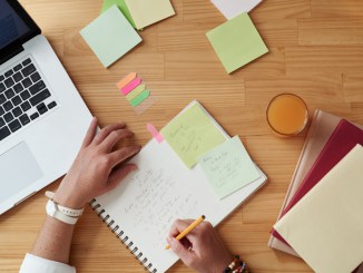 Person writing in notebook with laptop nearby