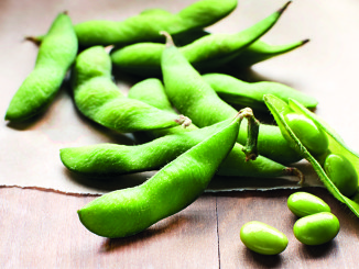 Shelled edamame on a wood background with a few shelled beans