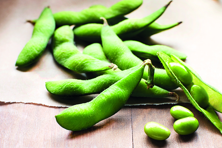 Edamame: A Baby Bean Comes Out of its Shell | Food & Nutrition | January February 2018 Shelled edamame on a wood background with a few shelled beans