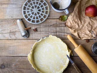 Empty unbaked crust surrounded by tools for baking a pie