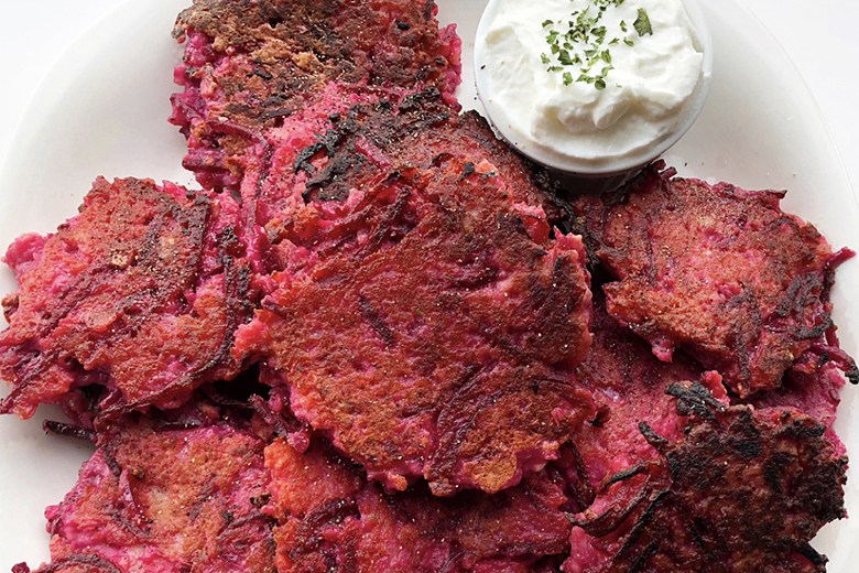 Pink Potato beet latkes with a dollop of sour cream on a plate