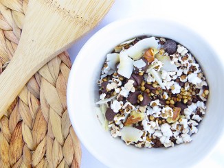 Popped Sorghum Trail Mix in white bowl next to a woven placemat and wooden spoon