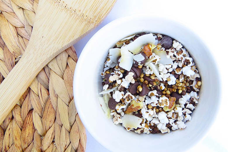 Sorghum, the Grain You Might Be Missing | Food & Nutrition | Stone Soup Popped Sorghum Trail Mix in white bowl next to a woven placemat and wooden spoon