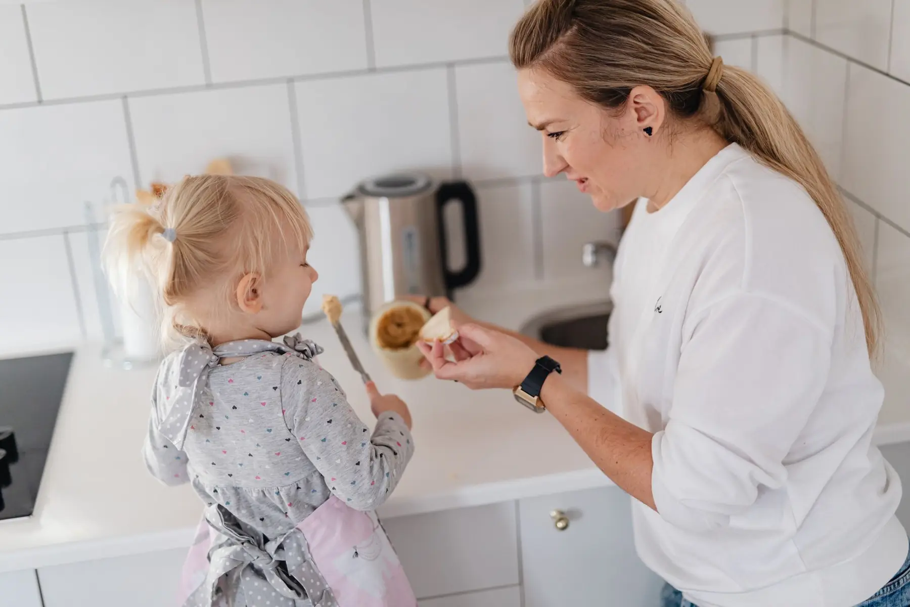 A mother and her young daughter interact while preparing food in a modern kitchen