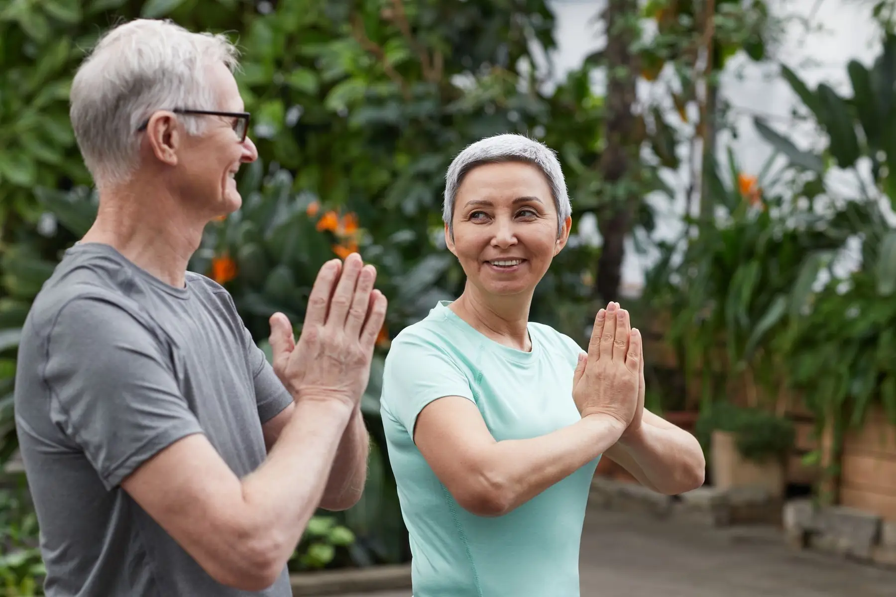 Happy senior couple practicing yoga in a lush greenhouse setting, embodying wellness and togetherness
