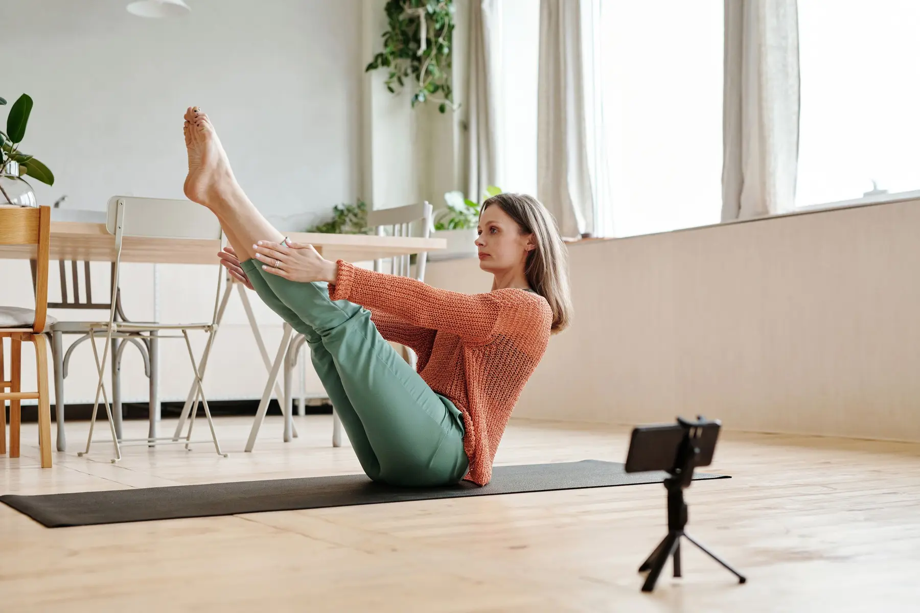 A woman does a pilates move on a mat in a sunny home