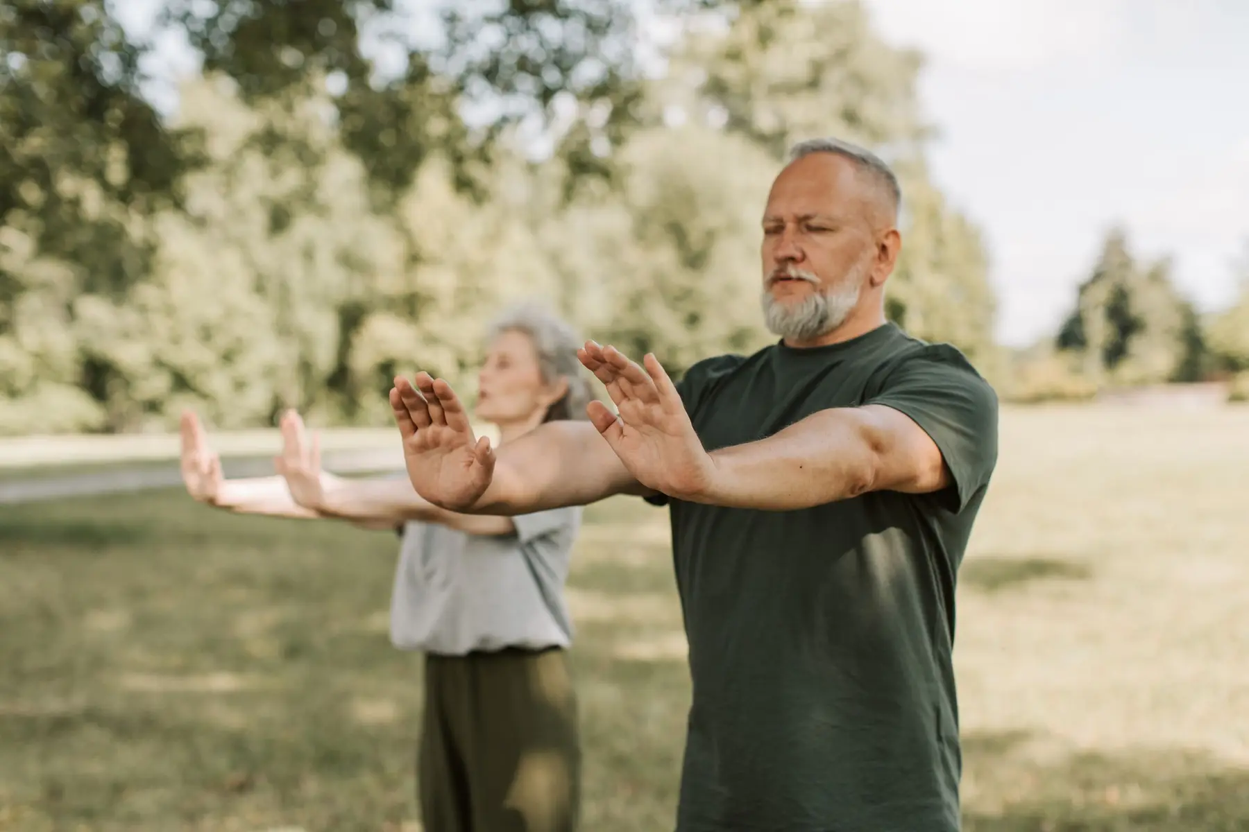 An older couple practice slow tai chi movements in a sunny park